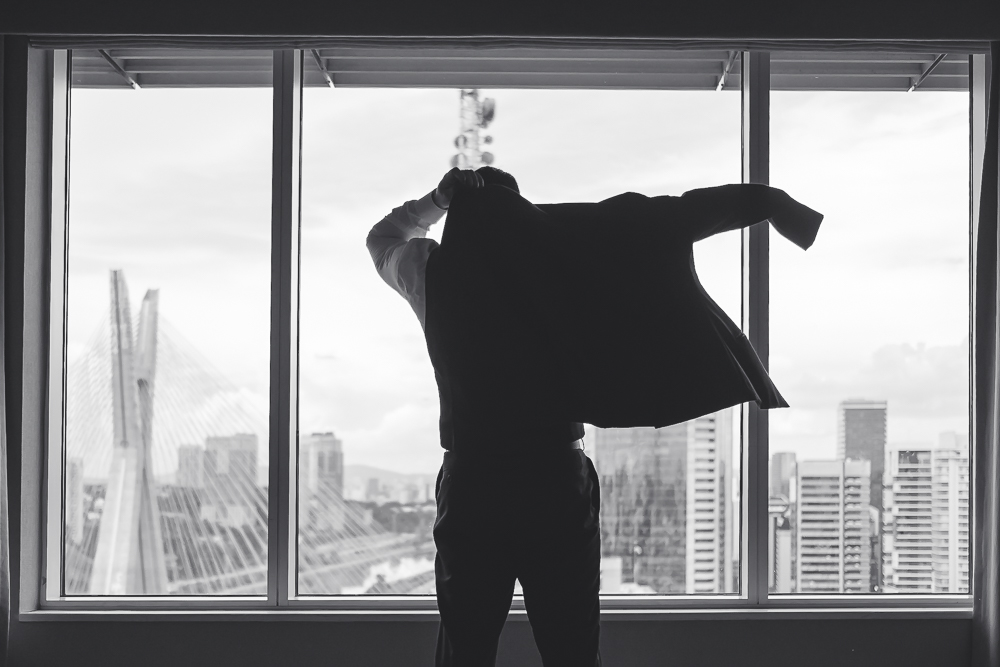 Noivo com terno de casamento se arrumando no quarto de hotel do Grand Hyatt São Paulo em frente a ponte estaiada em SP fotografado por Vinicius Donha fotografia