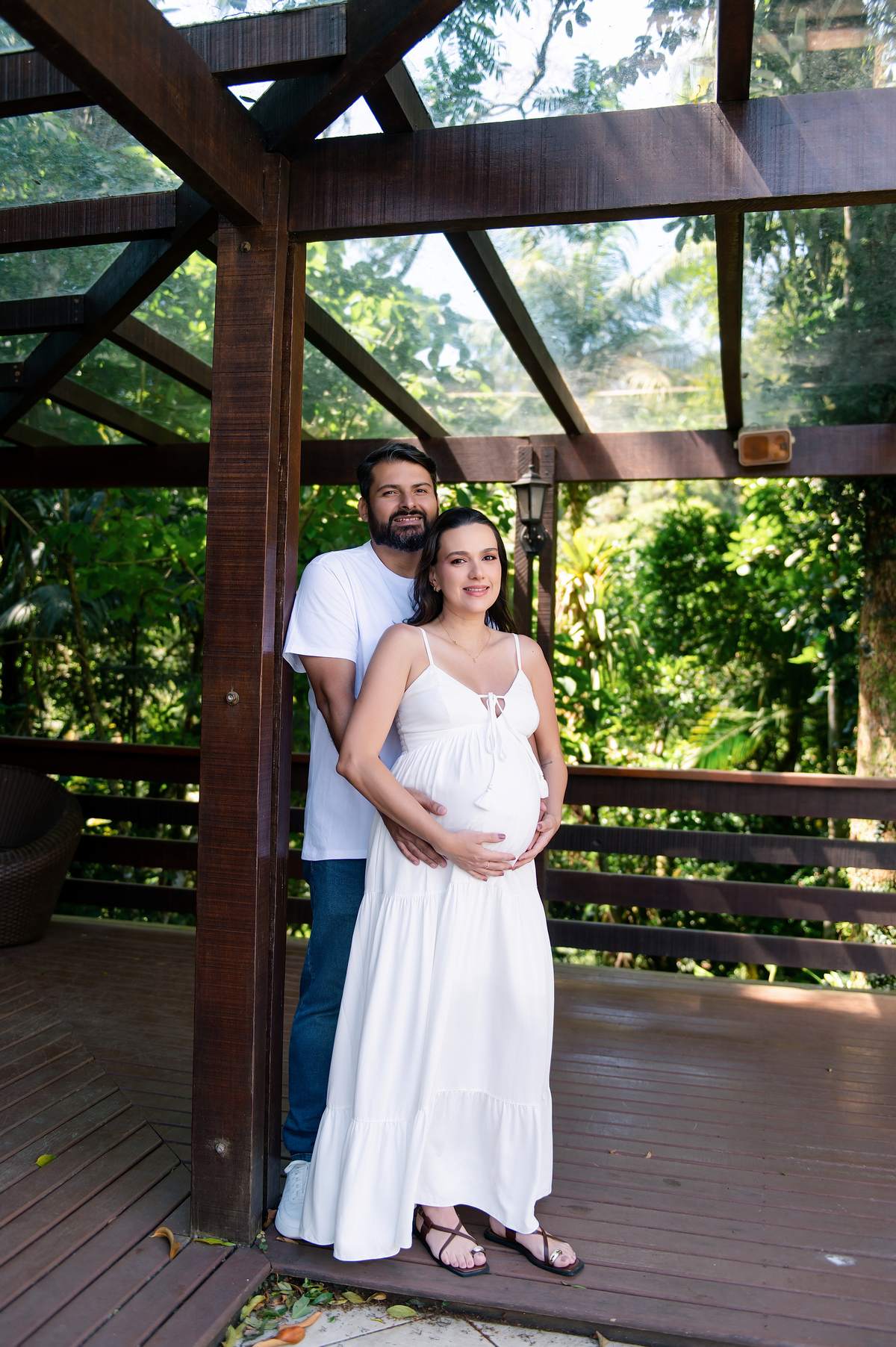 Marido e grávida na varanda coberta da Pousada Terê Parque, vestido branco