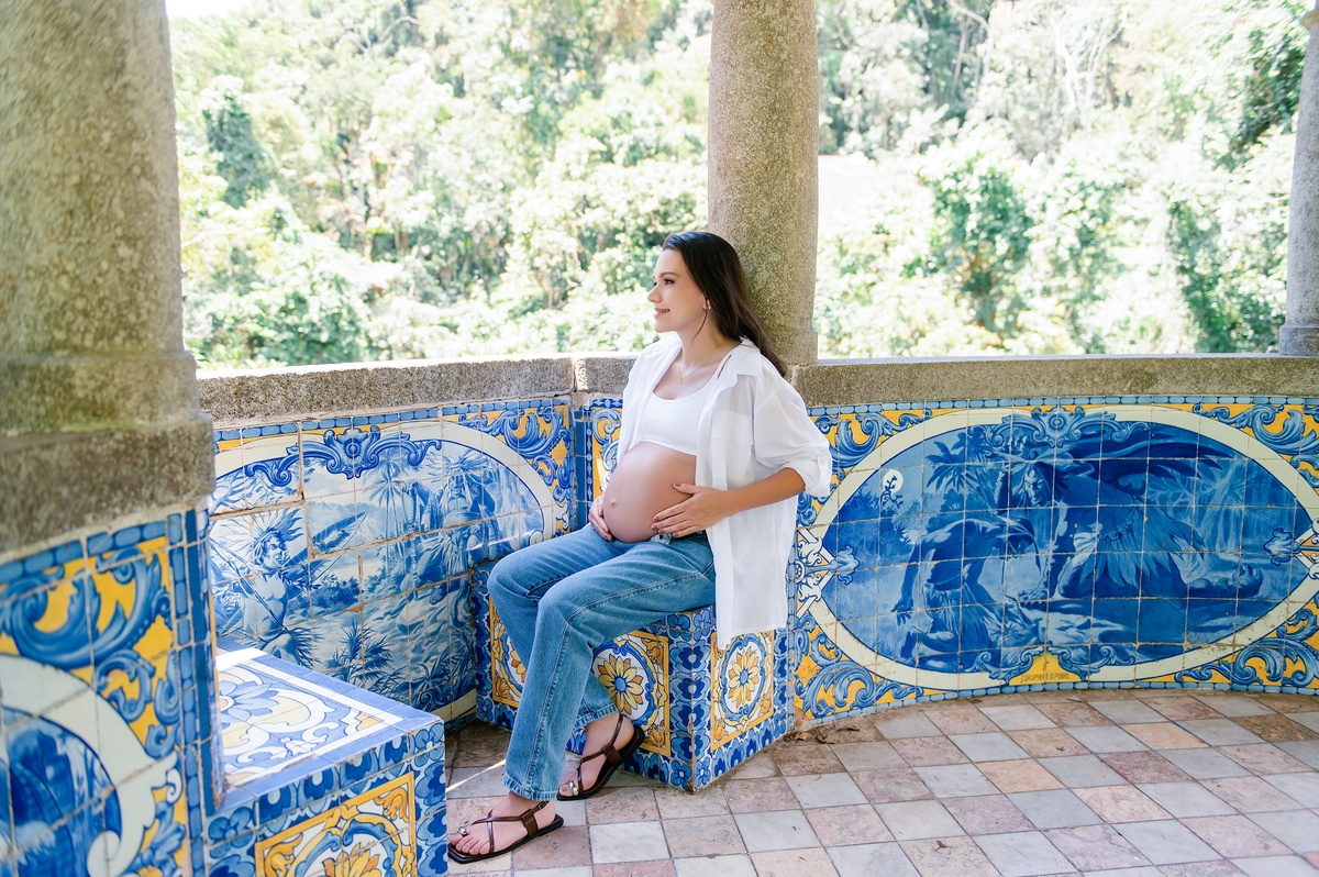 Gestante sentada no banco de azulejos da pousada, em pose contemplativa