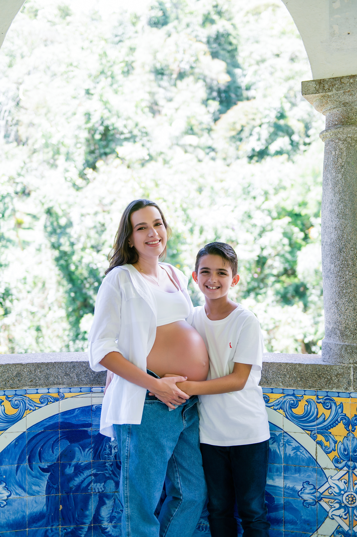 Mãe grávida e filho sorrindo juntos, com as mãos na barriga durante ensaio de gestação em Teresópolis