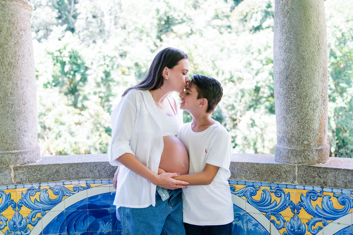 Mãe grávida e filho em momento de carinho, com fundo de azulejos com o PARNASO ao fundo