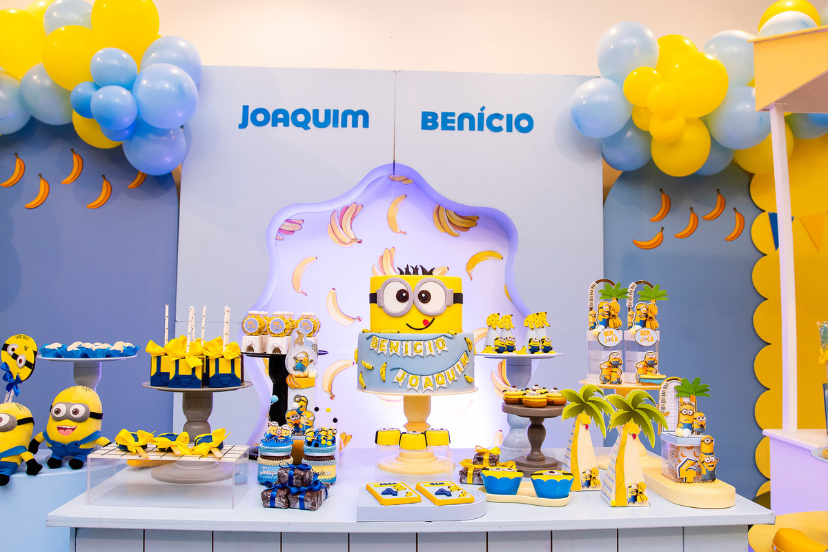 Cenografia temática Minions com foco nos detalhes do bolo e dos personalizados exclusivos da festa
