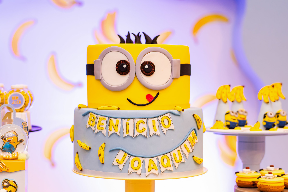 Cenografia temática Minions com foco nos detalhes do bolo e dos personalizados exclusivos da festa
