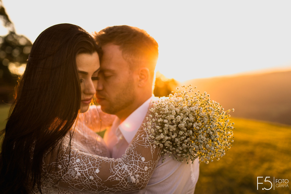 Noivos abraçados, buquê, pôr do sol