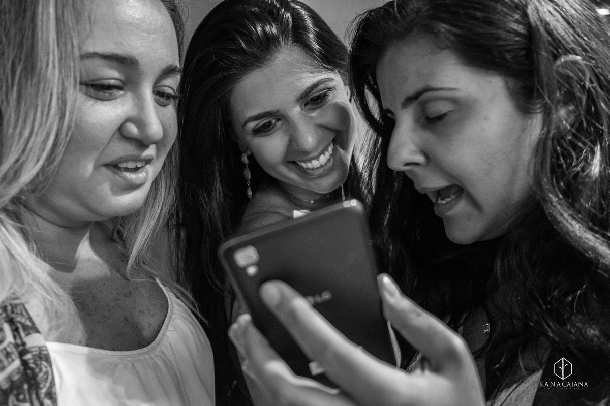 Noiva e amigas vendo foto no celular na pé do casamento