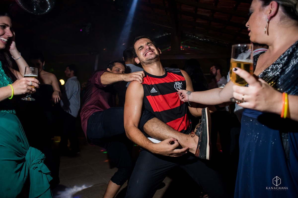 noivo brinca canta e toca guitarra usando perna de um convidado enquanto madrinha aperta seu peito durante festa do casamento no sítio casuarinas em Vargem Grande no rio de janeiro rj