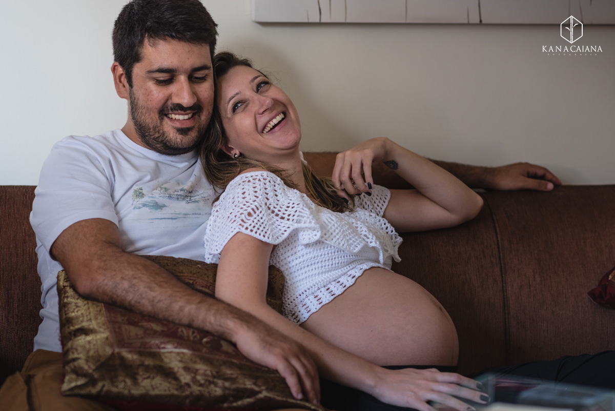 mulher gestante deitada no colo de seu marido no sofá de casa durante ensaio de fotos de gestante em São Paulo sp