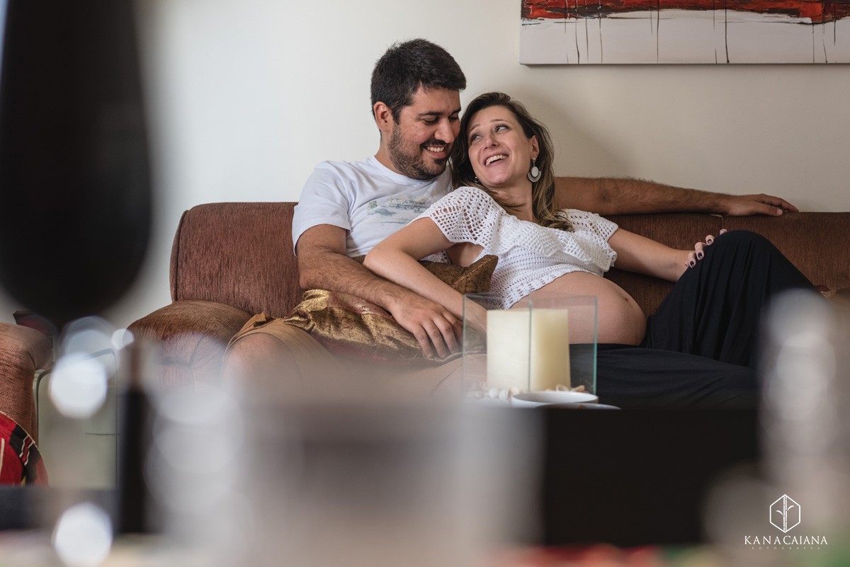 mulher gestante olha com carinho para seu marido no sofá de casa durante ensaio de fotos de gestante em São Paulo sp
