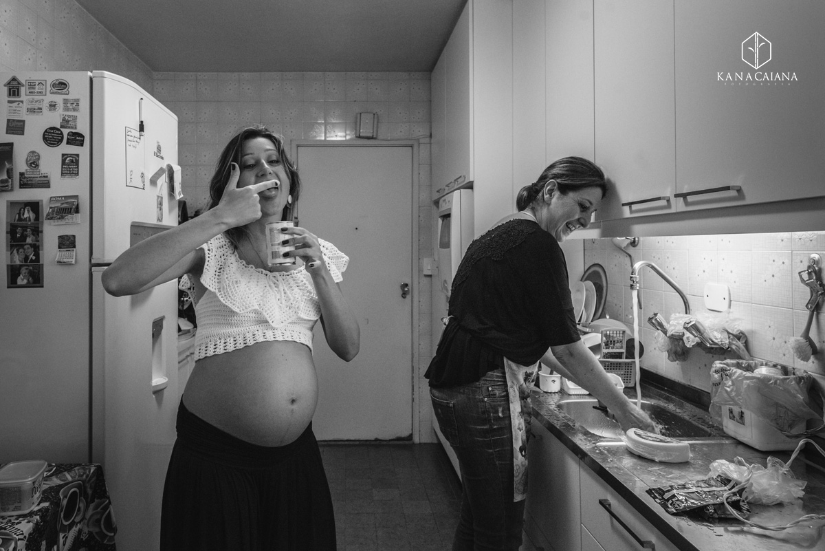 mulher grávida comendo leite condensado no dedo enquanto sua mãe lava a louça durante ensaio de fotos de gestante em São Paulo sp