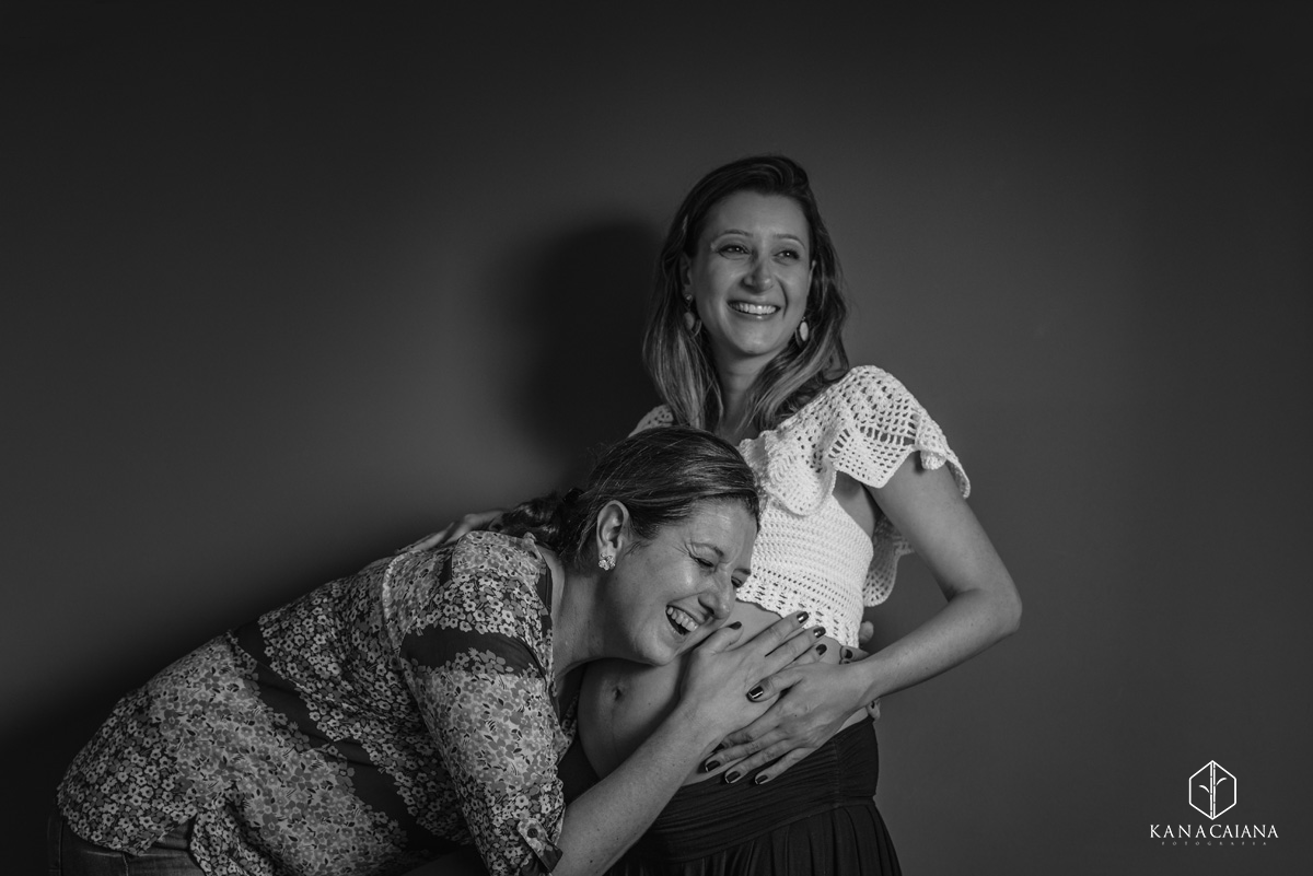 mãe coloca o ouvido na barriga de sua filha mulher grávida e sorri emocionada durante ensaio de fotos de gestante em São Paulo sp