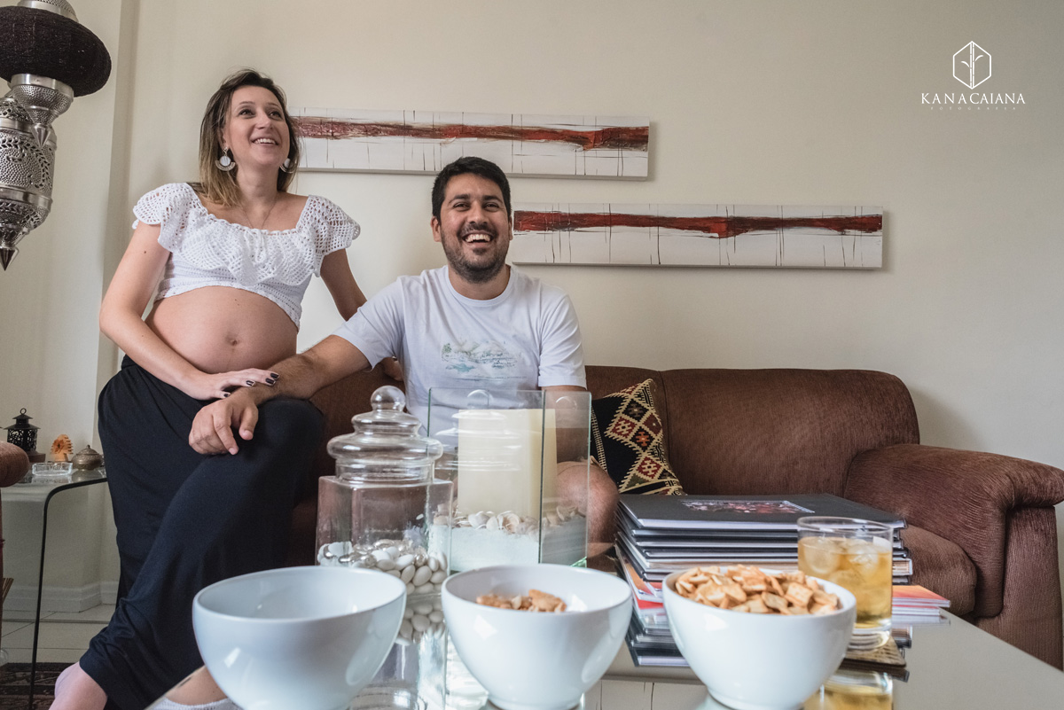 Mulher grávida e seu marido conversam no sofá de casa durante ensaio de fotos de gestante em São Paulo sp