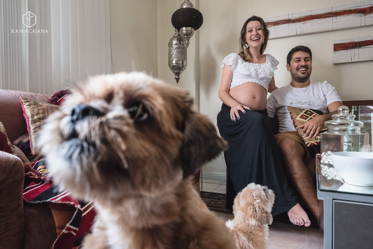 Mulher grávida e seu marido rindo enquanto seu cachorro curioso chega perto da câmera durante ensaio de fotos de gestante em São Paulo sp