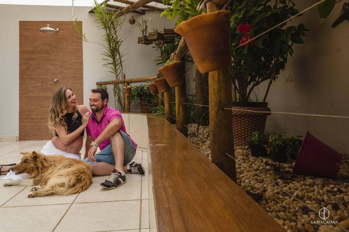 mulher grávida e seu marido sorriem junto com seu cachorro durante ensaio de fotos de gestante na cidade de lençóis paulista no interior de São Paulo sp