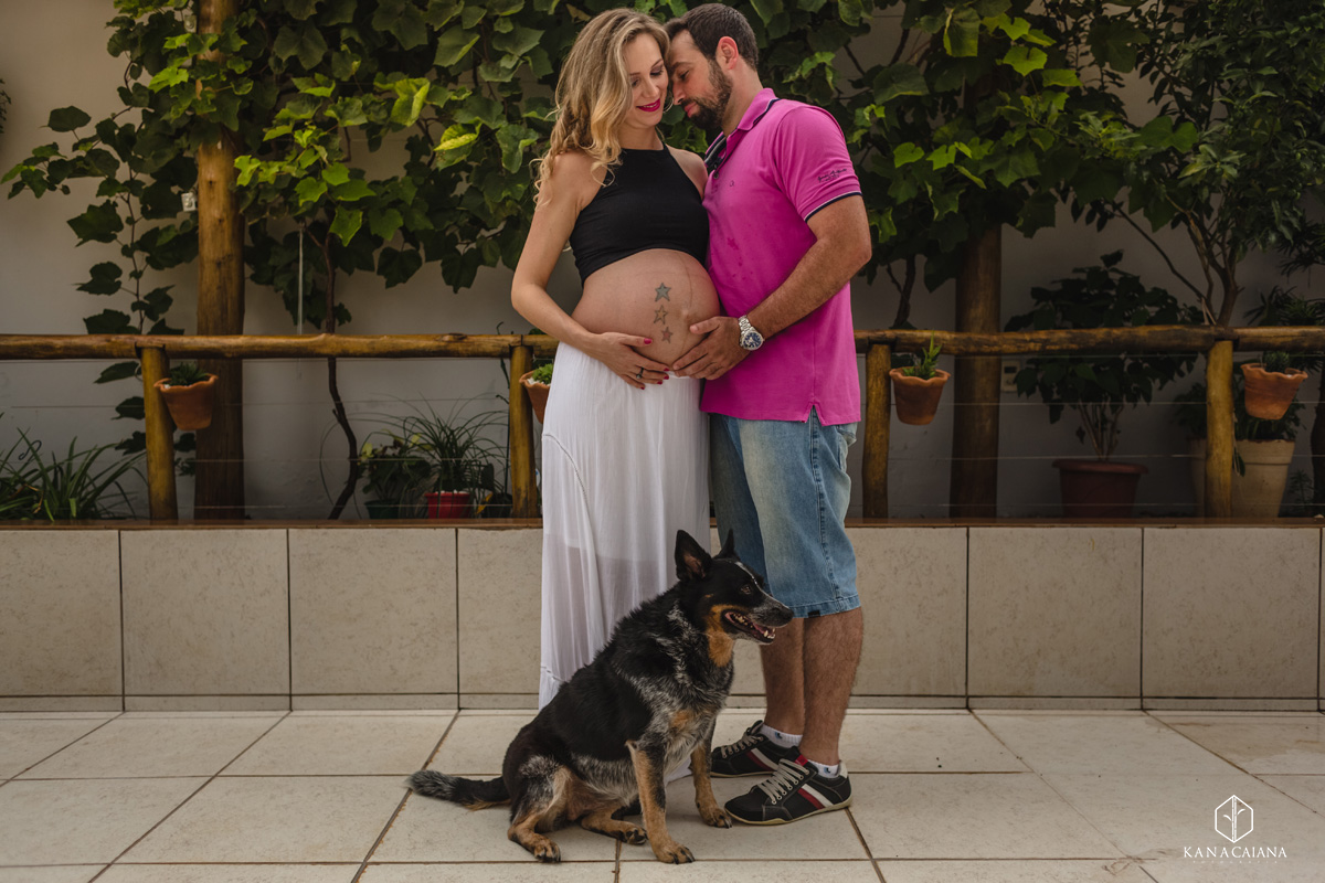 mulher grávida e seu marido fazem carinho na barriga se abraçam apaixonados cachorro senta aos seus pés durante ensaio de fotos de gestante na cidade de lençóis paulista no interior de São Paulo sp