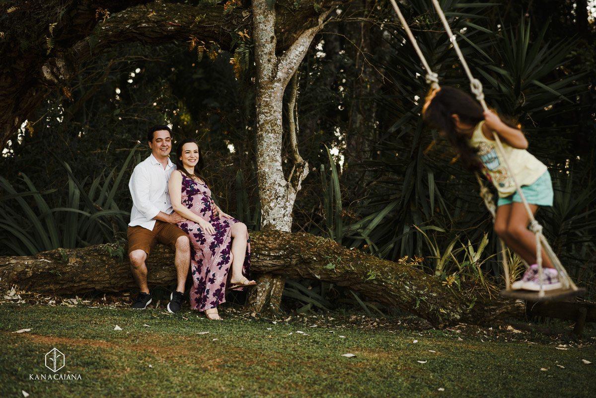 criança brincando no balanço  e casal posando para fotos em ensaio de gestante no campo