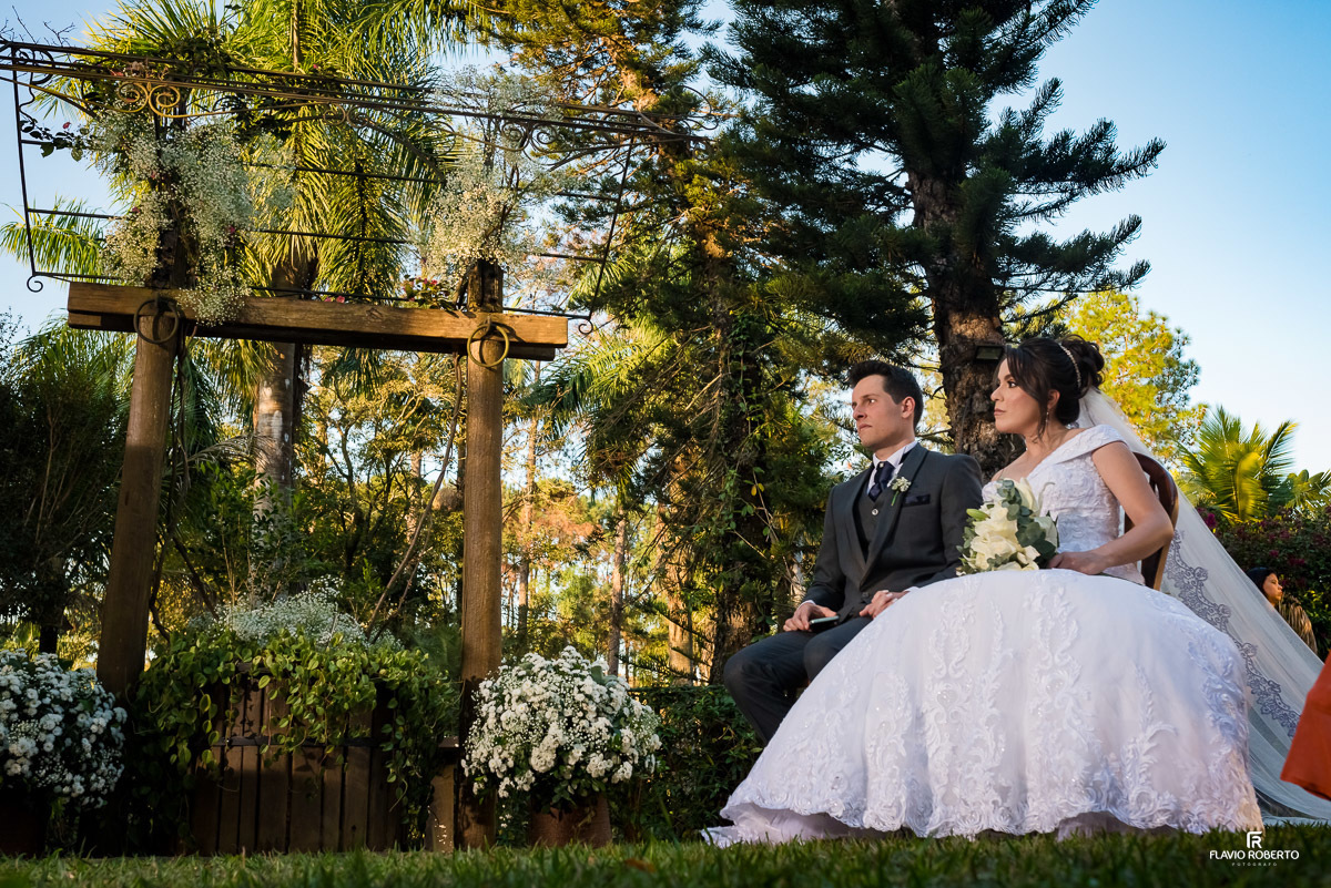 Noivos sentados juntos durante cerimônia do Casamento no Espaço Verde Vale em Taubaté-SP