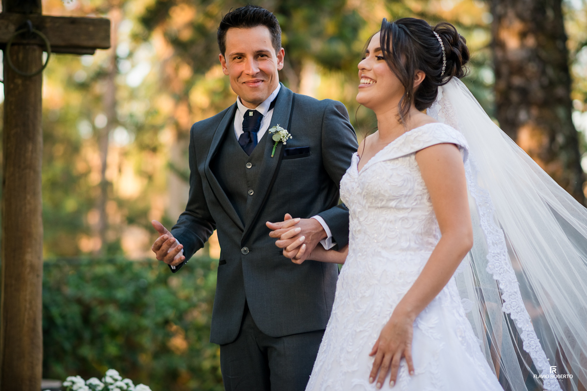 Casal de mãos dadas rindo,  juntos durante cerimônia do Casamento no Espaço Verde Vale em Taubaté-SP