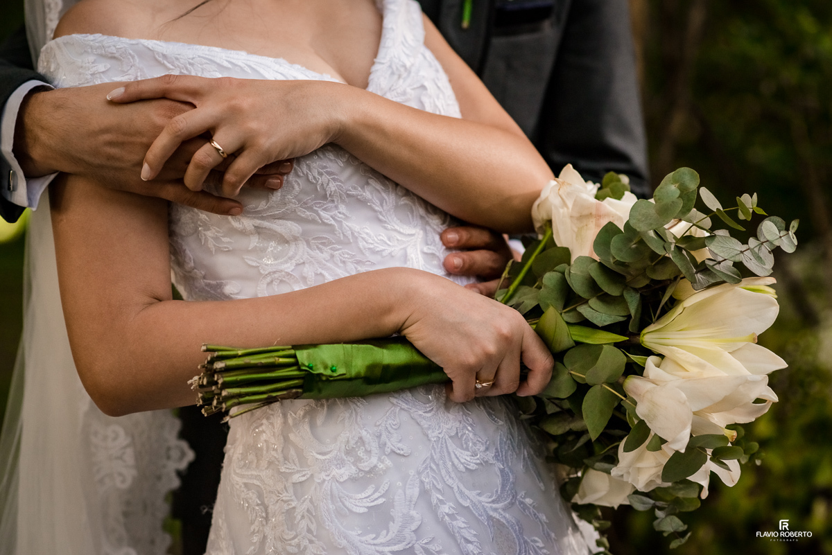 Noivo abraçando a Noiva de costas mostrando as alianças e o buquê durante Casamento realizado no Espaço Verde Vale em Taubaté-SP
