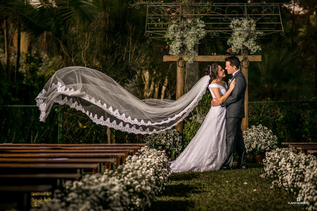 Noivos abraçados com o véu da noiva voando durante Casamento no Espaço Verde Vale em Taubaté