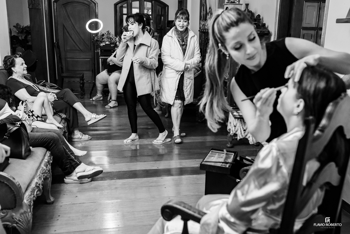 Noiva sendo maquiada em uma sala com as madrinhas em casamento em Lorena/SP