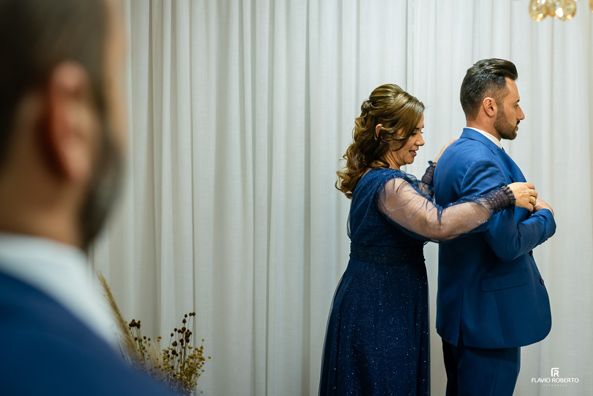 Mãe do Noivo colocando seu paletó durante o making of no Espaço Luxo em Taubaté