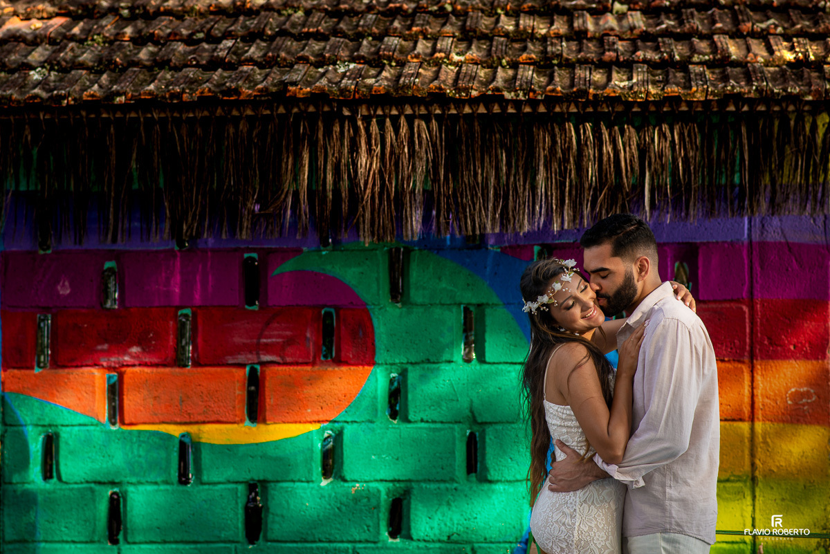 Noivos abraçados do lado de uma parede colorida de Quiosque, durante ensaio pre wedding em Ilhabela