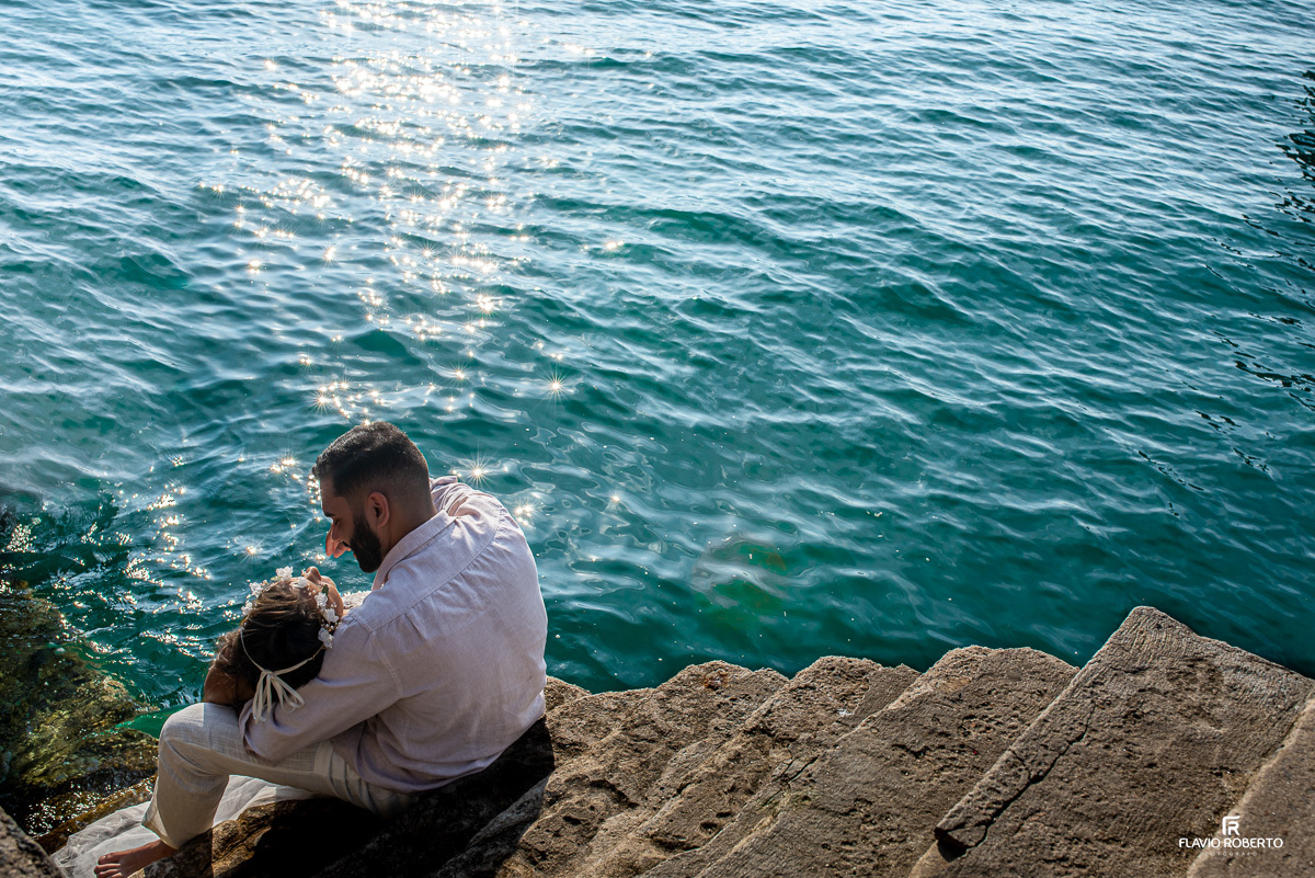 noiva deitada nas pernas do noivo, sentado em uma escada do lado do mar, durante ensaio pre wedding em Ilhabela