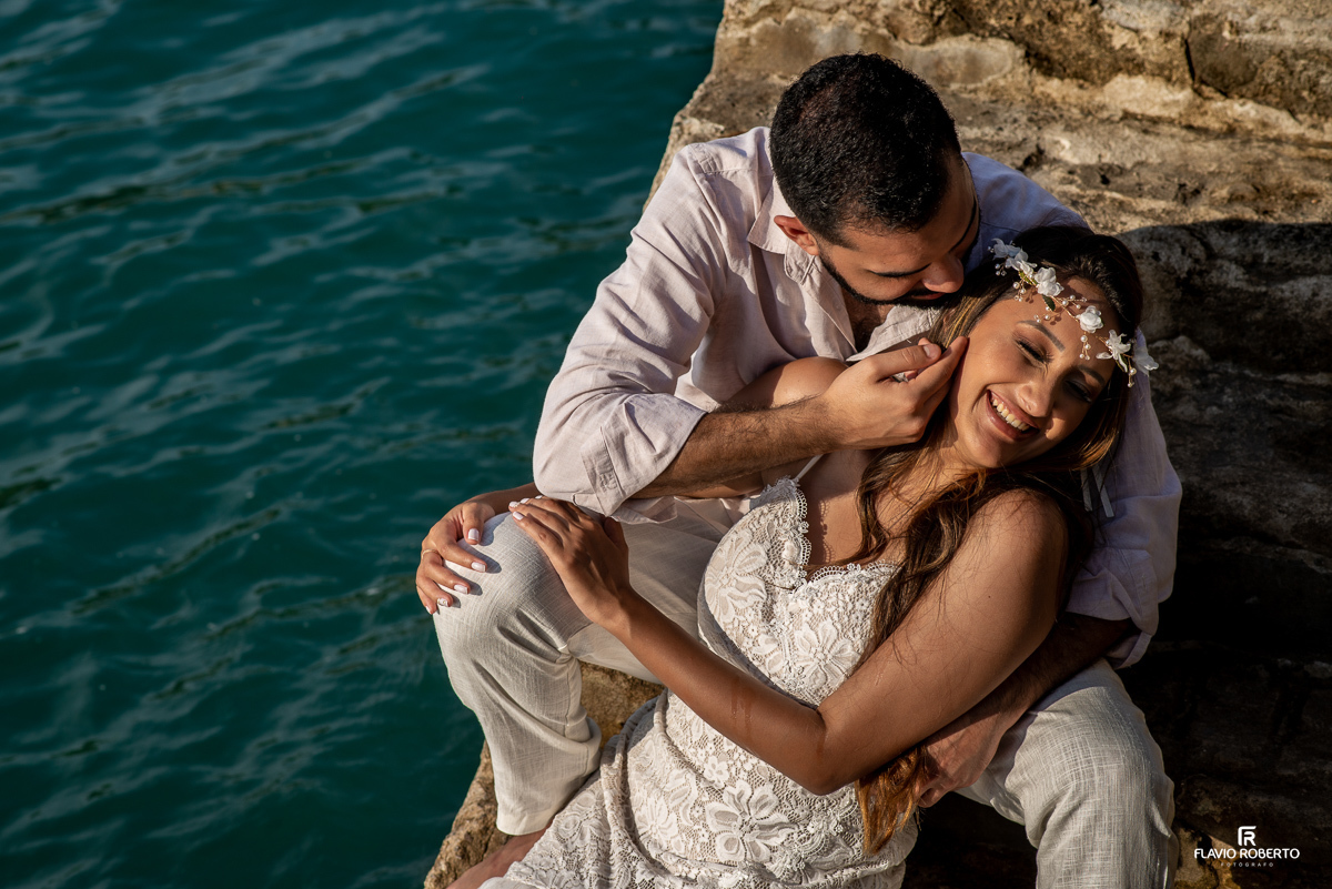 noiva deitada nas pernas do noivo, que está fazendo carinho nela, sentados em uma escada do lado do mardurante ensaio pre wedding em Ilhabela
