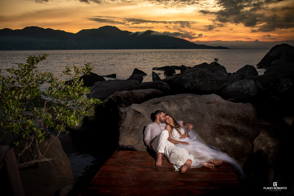 noivos deitados em um deck entre as pedras do lado do mar, durante ensaio pre wedding em Ilhabela