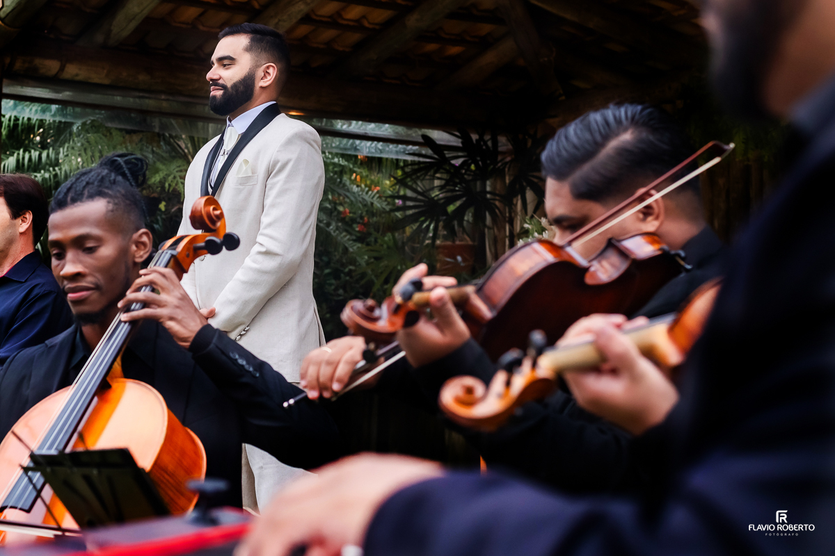 noivo esperando a Noiva chegar escutando os músicos tocarem no seu Casamento no Rancho Mustang em Pindamonhangaba.
