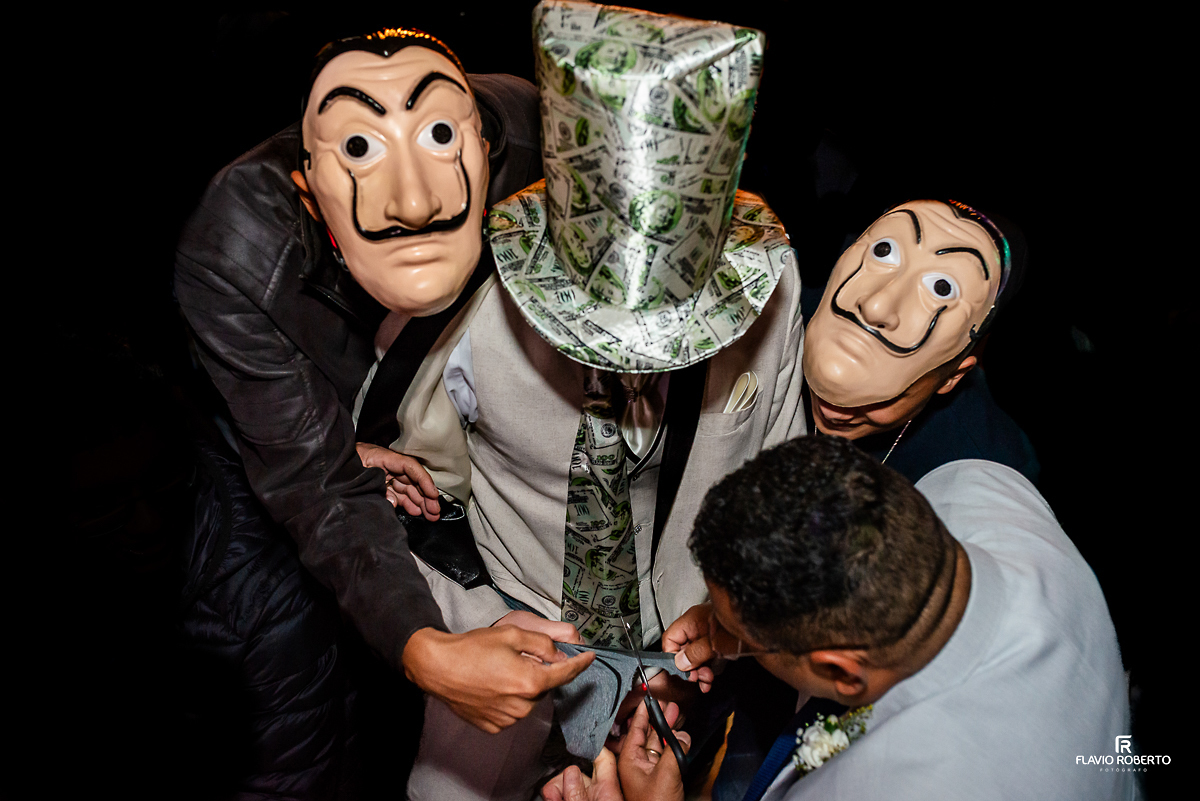 Noivo passando a gravata com seus padrinhos com máscaras da Casa de Papel, durante Casamento no Rancho Mustang em Pindamonhangaba.