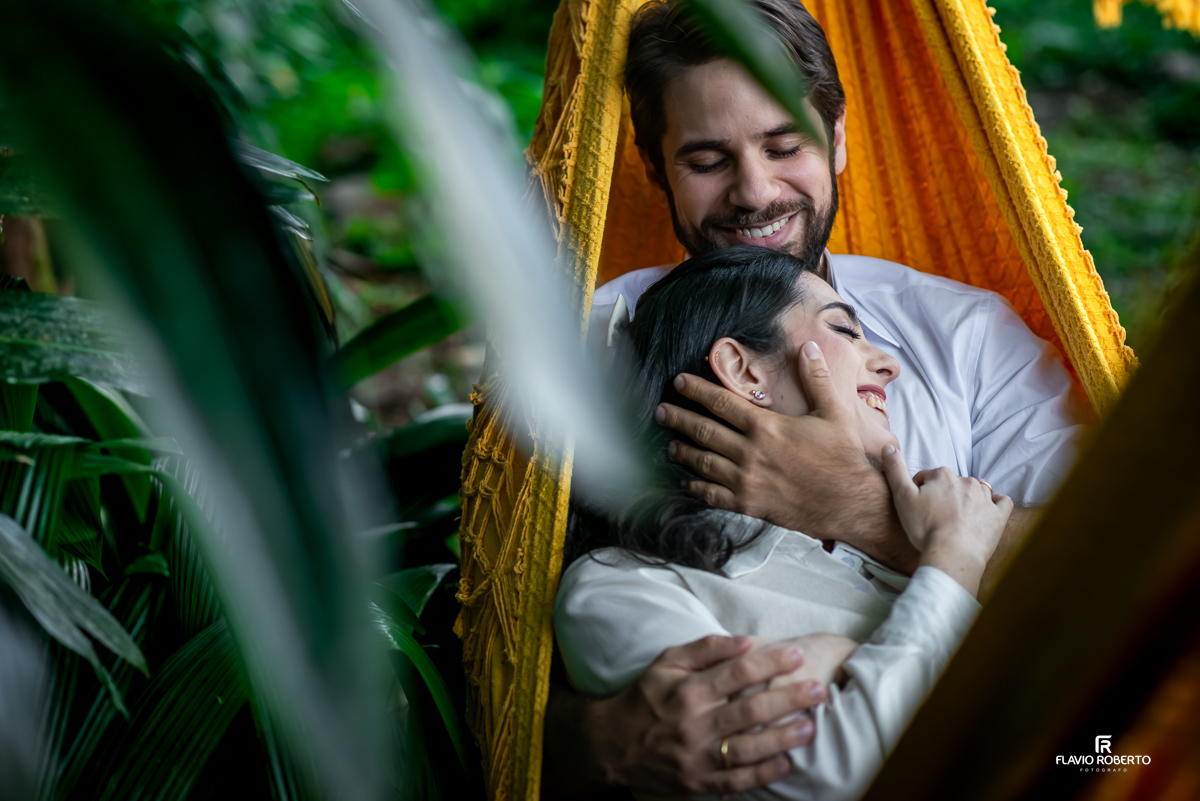 Casal sorridente e abraçado em rede amarela, transmitindo conexão e aconchego em meio ao verde do Restaurante La Família