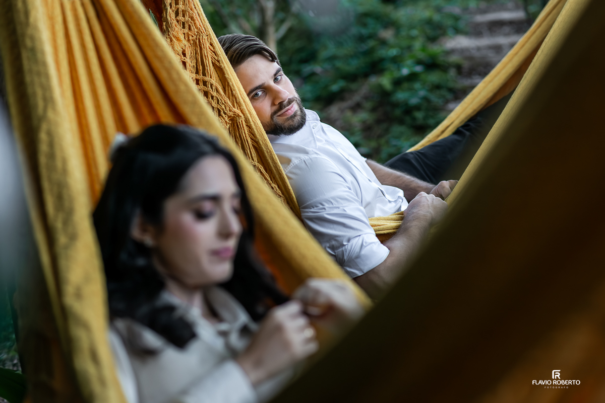 Laís deitada na rede amarela olhando com ternura para Gabriel, em primeiro plano desfocado, capturando a cumplicidade do casal.