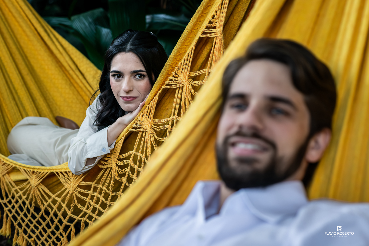 Laís deitada na rede amarela olhando com ternura para Gabriel, em primeiro plano desfocado, capturando a cumplicidade do casal.