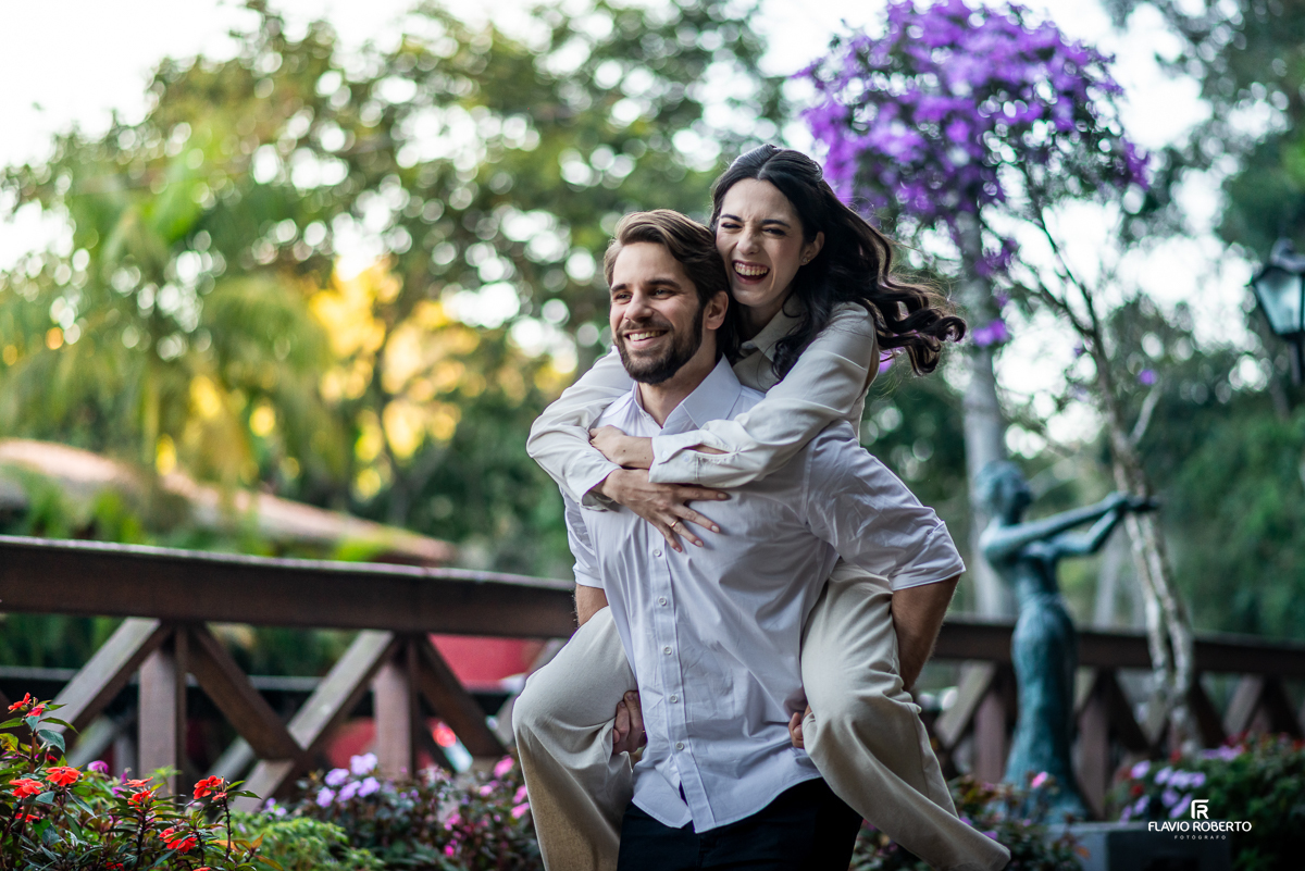 Laís dá uma gargalhada nas costas de Gabriel, que a carrega nas costas em um momento leve e divertido entre flores e natureza.