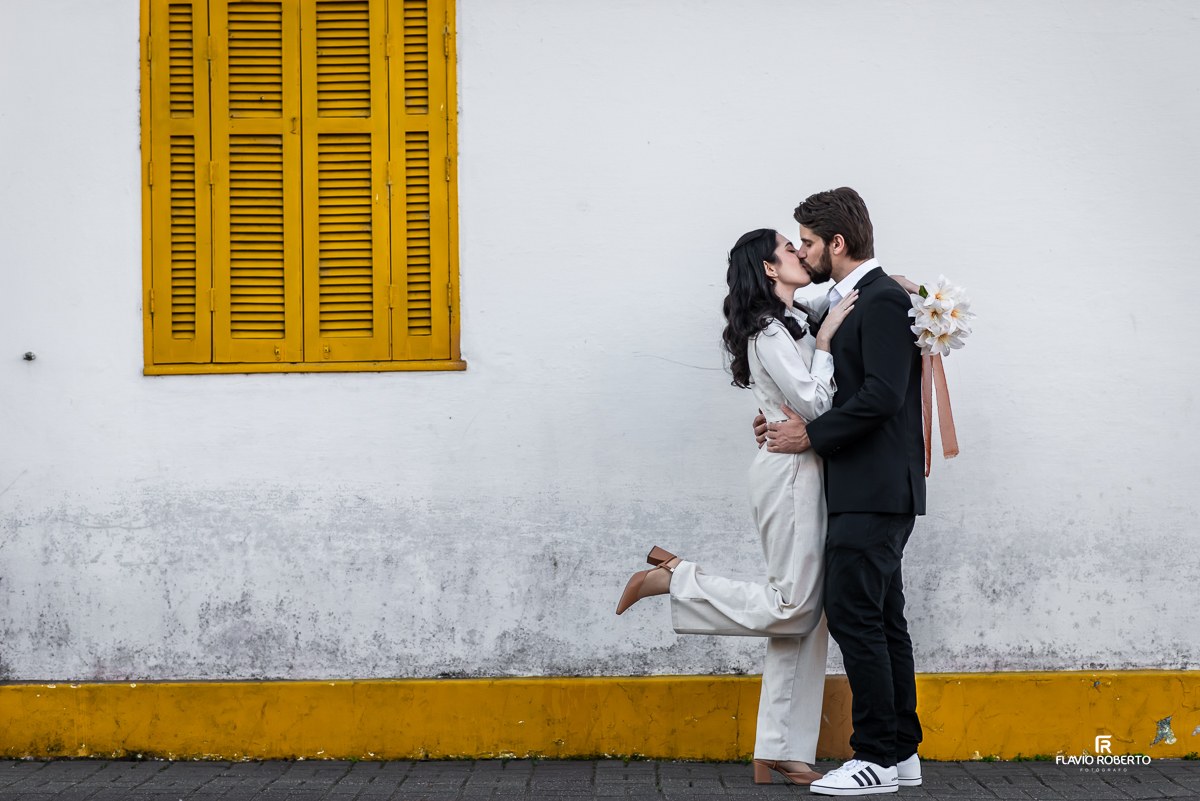 O casal abraçado em frente a uma charmosa casa no centro de Santo Antônio do Pinhal.