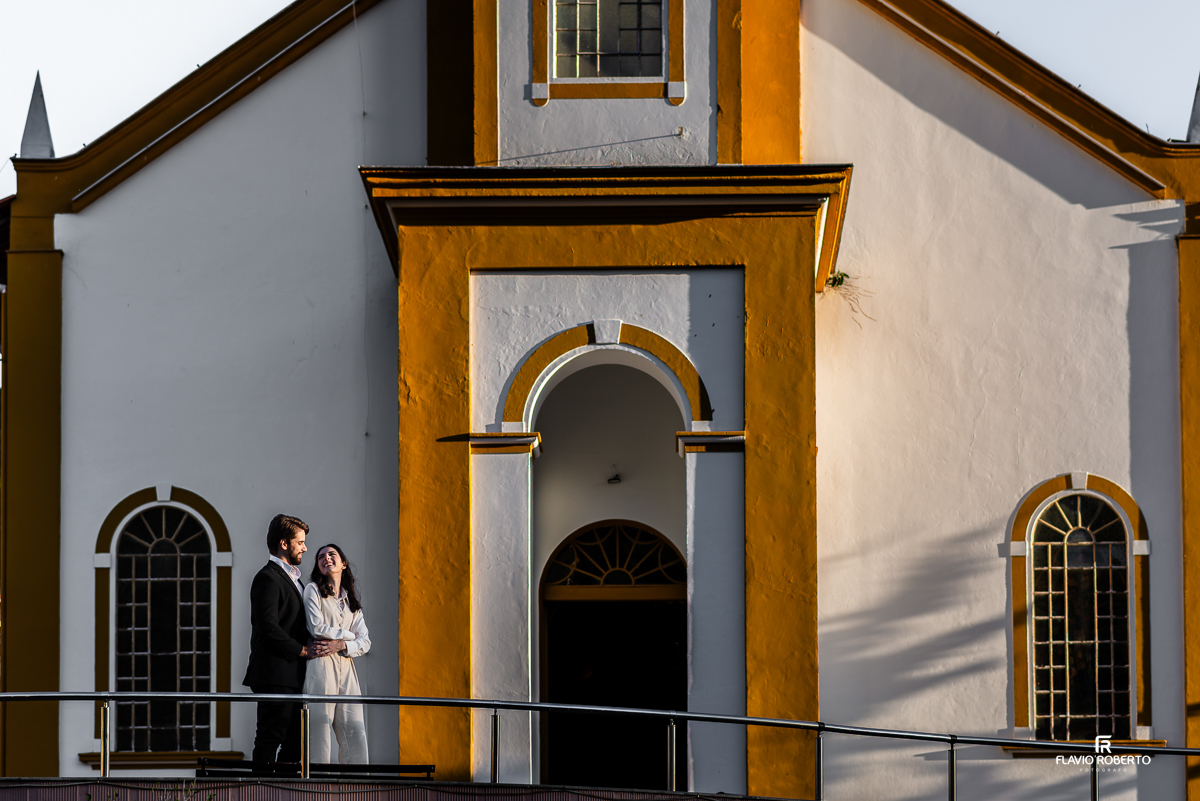 Casal em clima de romance em frente à charmosa fachada colonial de uma igreja em Santo Antônio do Pinhal, sob a luz dourada do entardecer