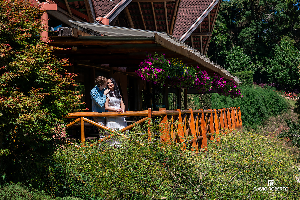 Casal em ensaio pré casamento no Jardim dos Pinhais em SP, abraçados na varanda cercada por flores e natureza.