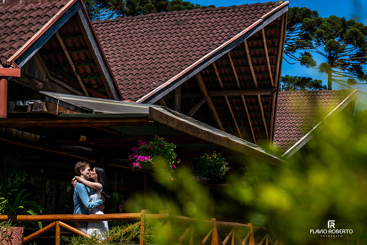 Ensaio pré casamento no Jardim dos Pinhais em SP, casal se beijando em chalé de madeira com flores pendentes.