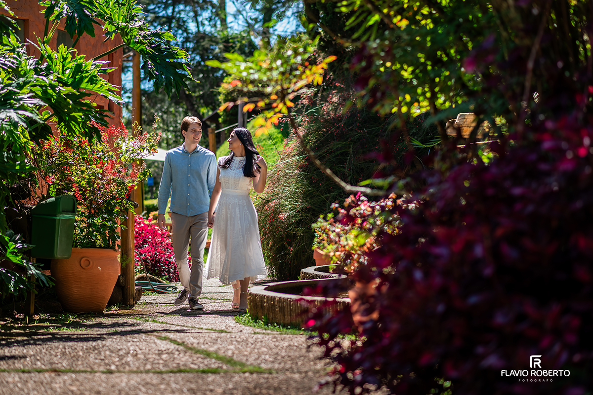 Casal caminhando entre jardins floridos em ensaio pré casamento no Jardim dos Pinhais em SP.