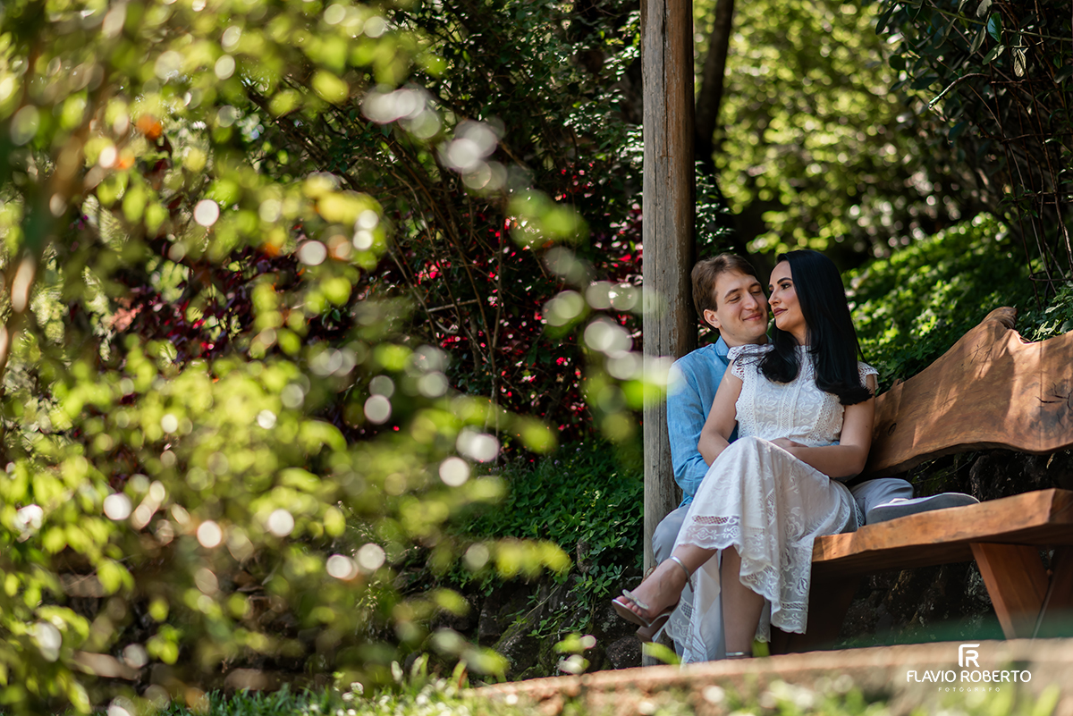 Casal sentado em banco de madeira em ensaio pré casamento no Jardim dos Pinhais em SP, cercados por verde.