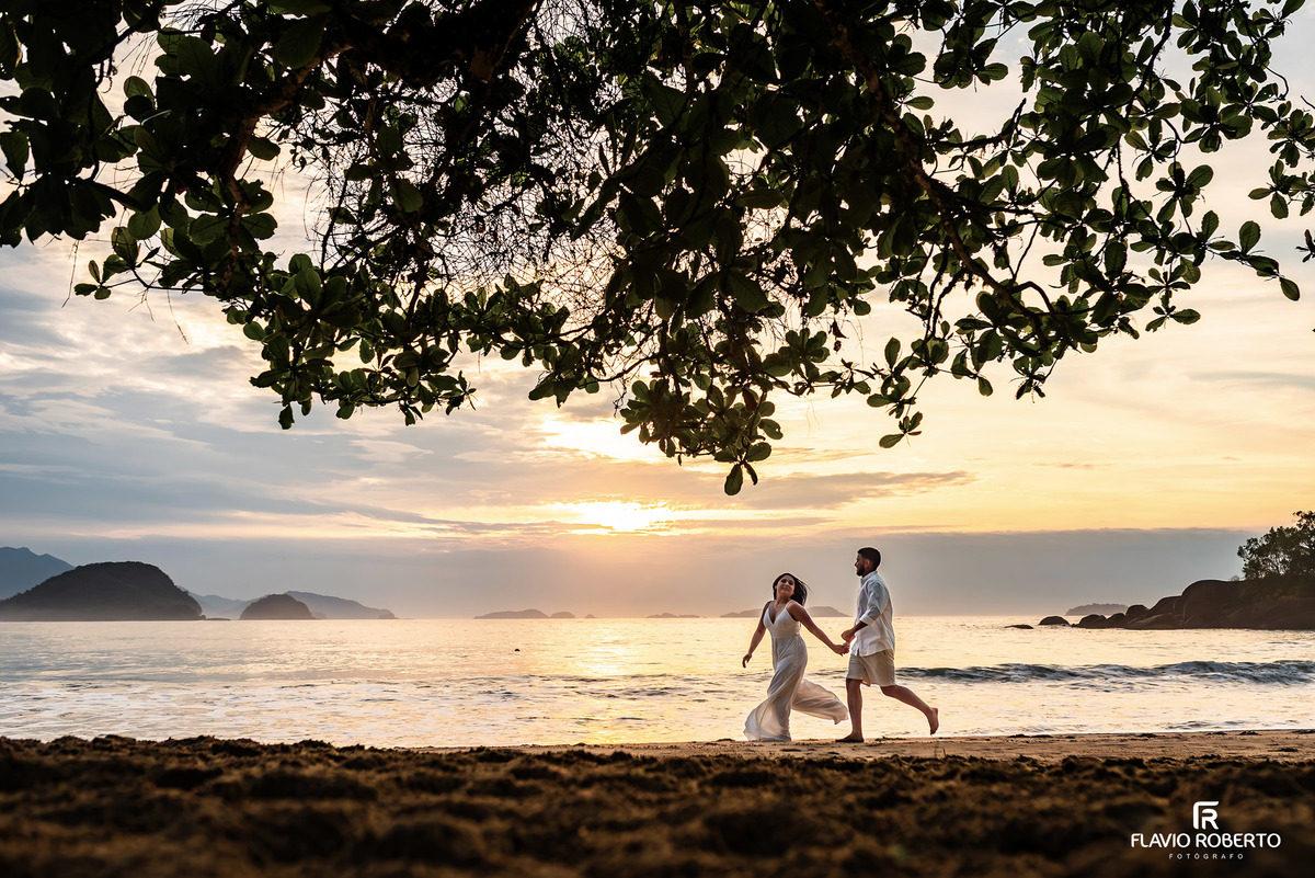 Ensaio pré casamento na Praia de Ubatuba com casal caminhando à beira-mar durante o nascer do sol, fotografia natural e conexão verdadeira