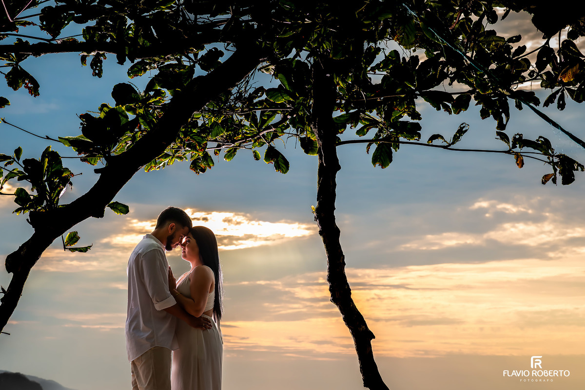 Ensaio pré casamento na Praia de Ubatuba ao nascer do sol com casal abraçado sob árvores, fotografia natural e romântica