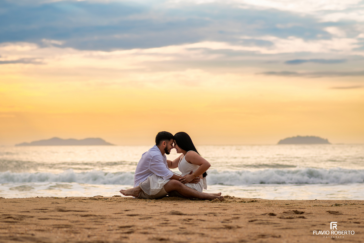 Ensaio pré wedding na praia de Ubatuba ao nascer do sol com casal sentado na areia, fotos naturais e espontâneas