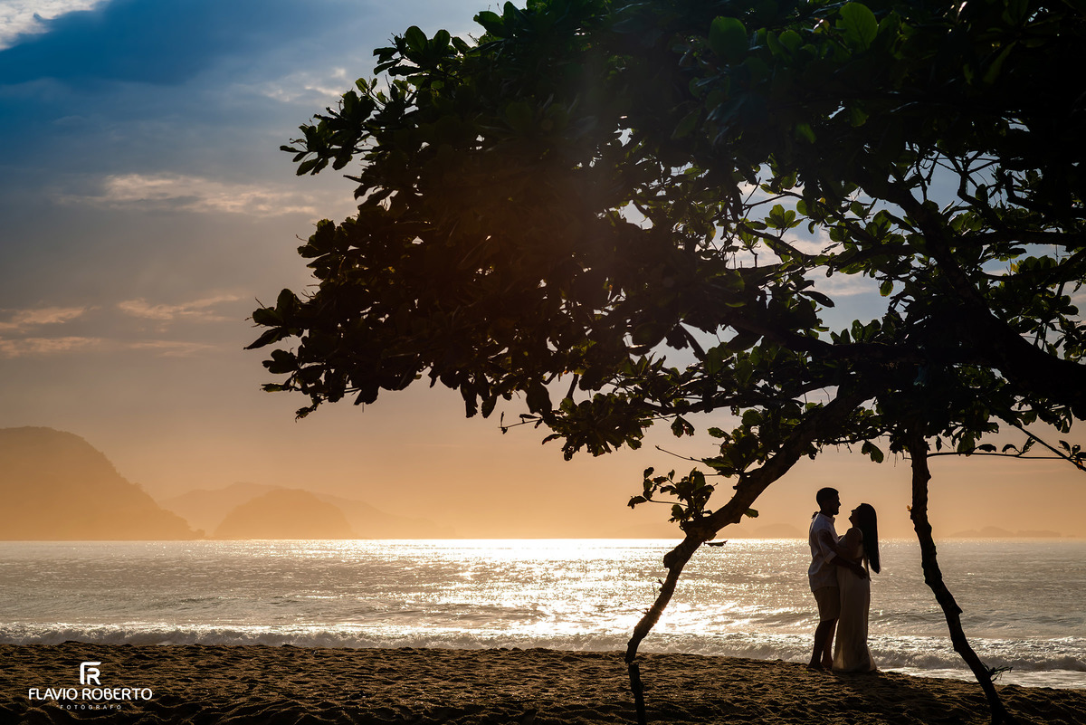 Silhueta de casal em ensaio pré casamento na Praia de Ubatuba ao nascer do sol, luz dourada e emoção verdadeira