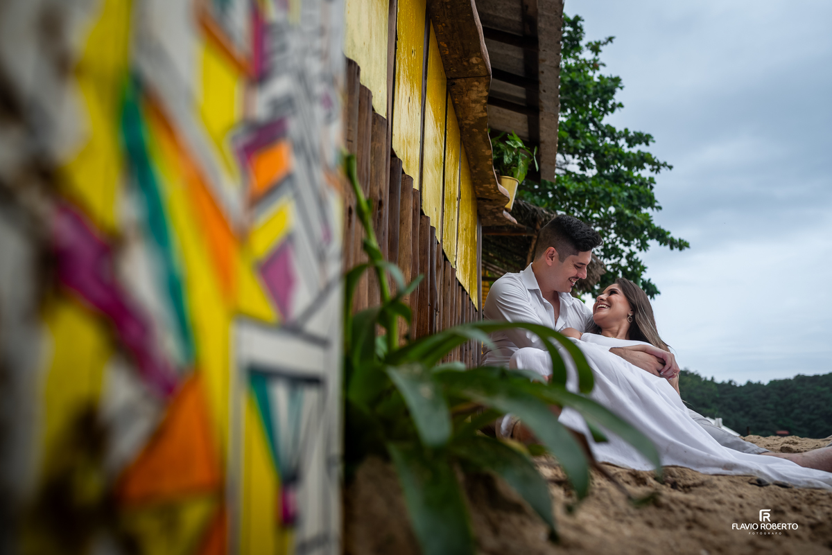 Ensaio pre wedding em Ubatuba com casal relaxando na areia em cenário rústico de praia, fotografia leve e cheia de conexão