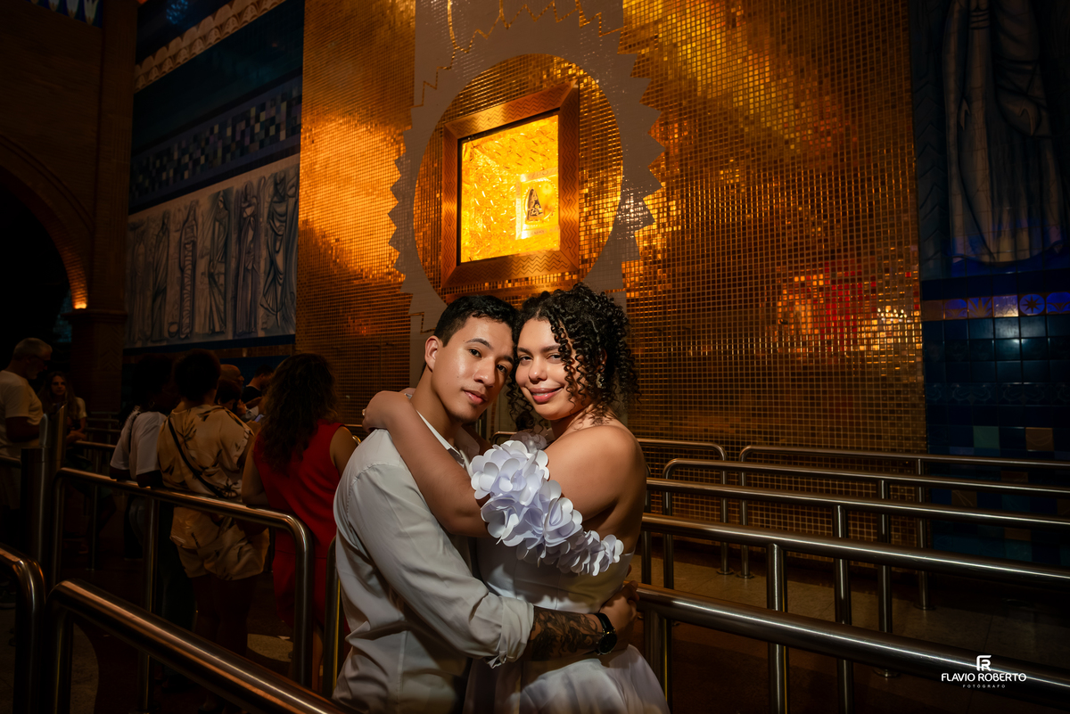 Casal em ensaio pré wedding diante da imagem de Nossa Senhora Aparecida com iluminação dourada