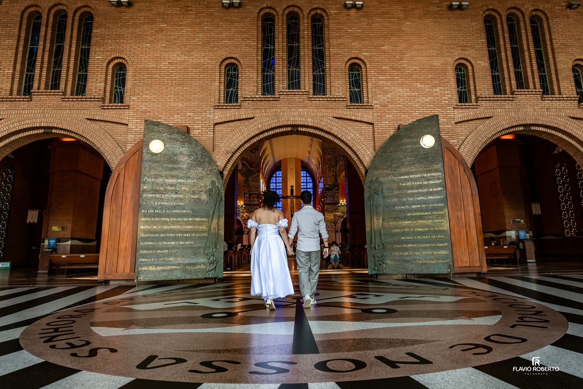 Casal entrando no Santuário Nacional de Aparecida pela Posta Santa de mãos dadas durante ensaio pré wedding