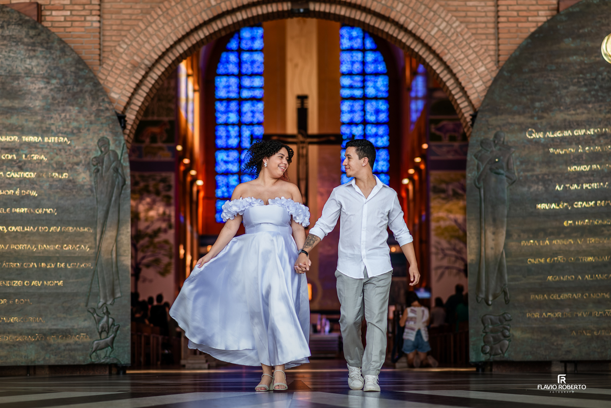 Casal caminhando no interior do Santuário Nacional de Aparecida durante ensaio pré wedding com vitrais ao fundo