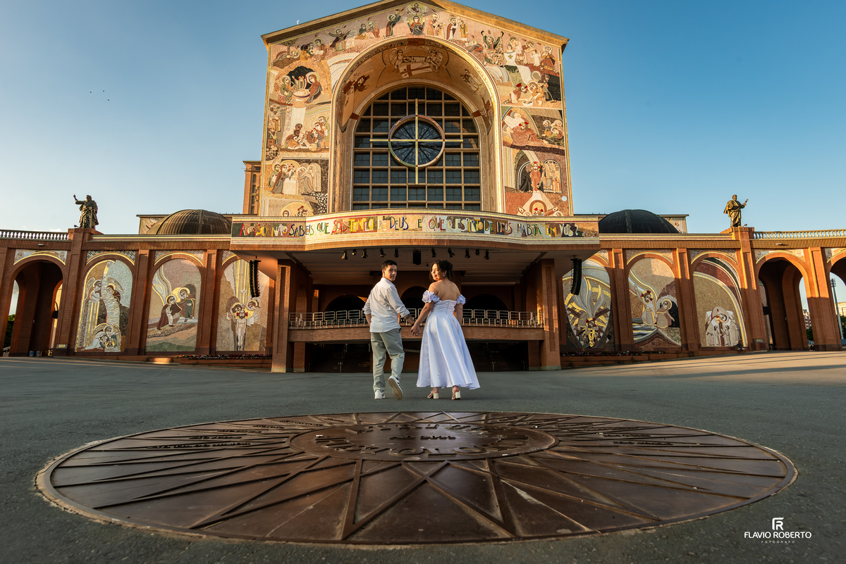 Casal caminhando em direção ao Santuário Nacional de Aparecida durante ensaio pré wedding com fachada imponente